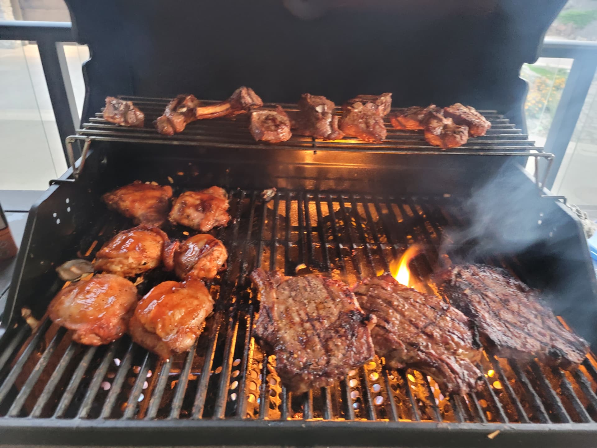 A loaded grill with lamb chops, chicken thighs and steaks over open flame